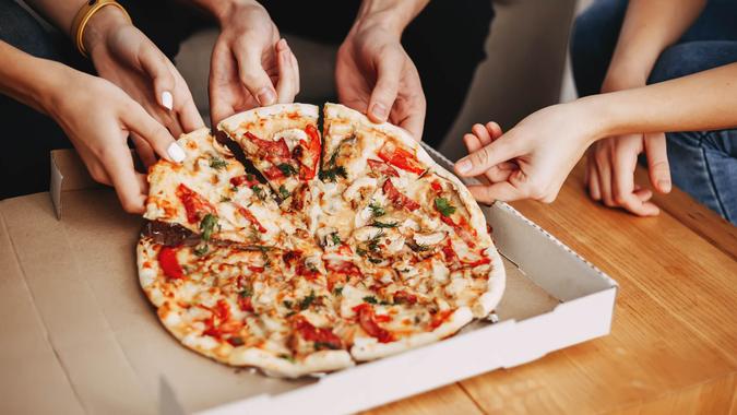 Hands of young people taking pizza slices from delivery box dining together, millennial friends sharing meal having lunch at home, food delivery concept.