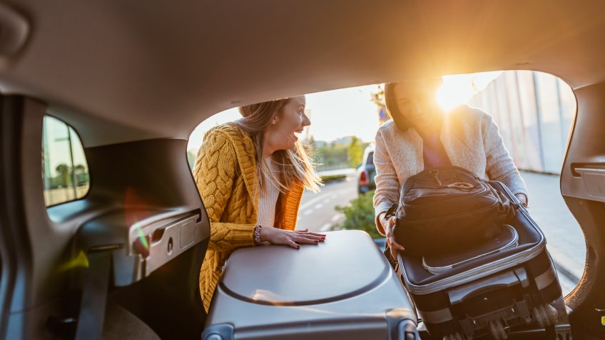Two women tourists loading a heavy bag into the back of an estate car with the boot open.
