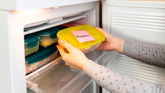 Woman taking container with frozen mixed vegetables out from freezer.