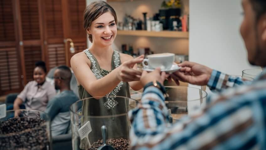 Smiling young woman receiving coffee from barista in a trendy coffee cafe.