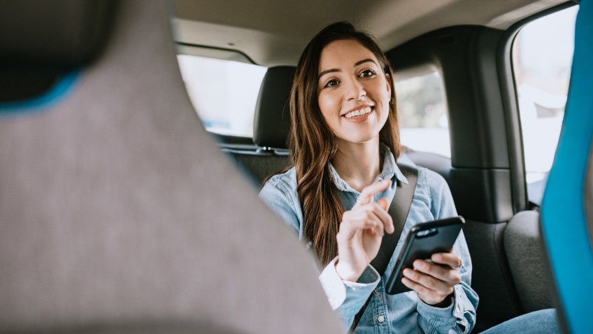 A Latina business woman rides in a crowdsourced taxi, having requested a pick up and drop off on her smartphone.
