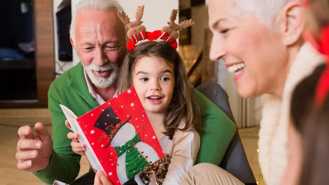 Joyful older couple reading Christmas card to their granddaughters.