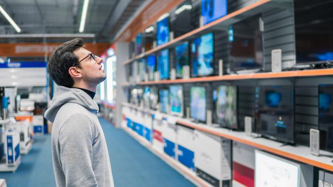 Smart modern male customer choosing large TV-sets at electronics store.