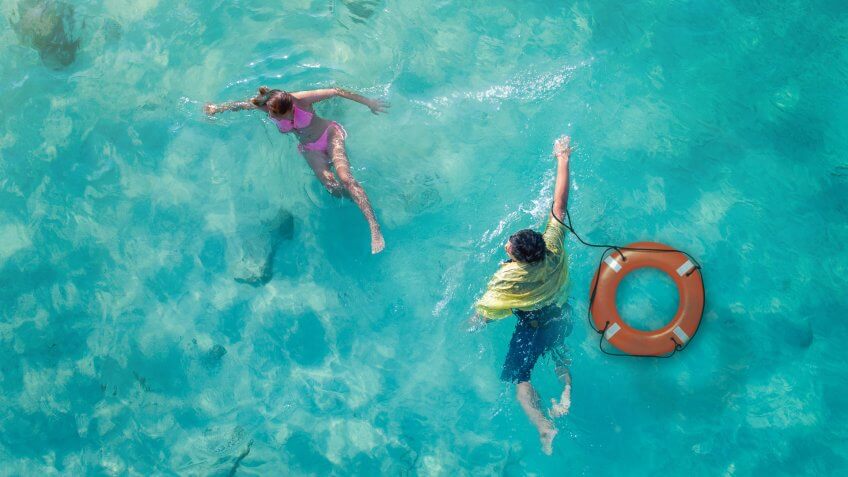 Aerial top view an emergency helping the woman drowning swim in the sea by man jumping to the sea with lifebouy, cramp in water of the woman need swift assistant.