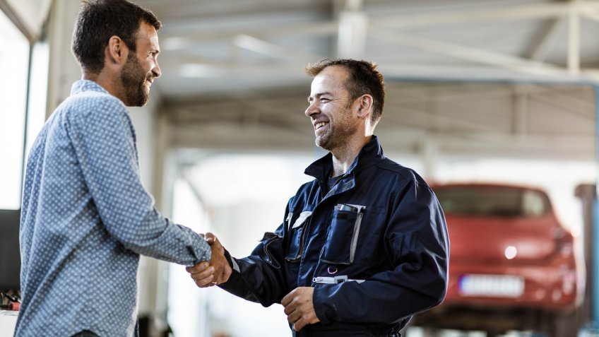 Happy mechanic came to an agreement with his customer in auto repair shop.