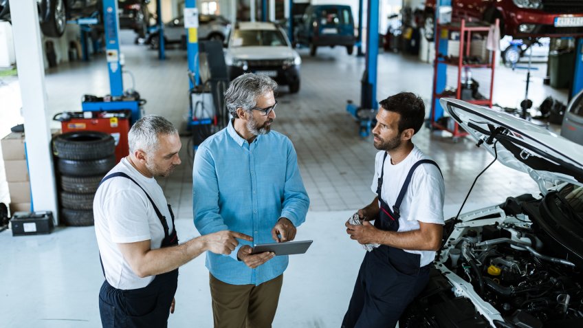 Mid adult manager using digital tablet while talking to mechanics in auto repair shop.