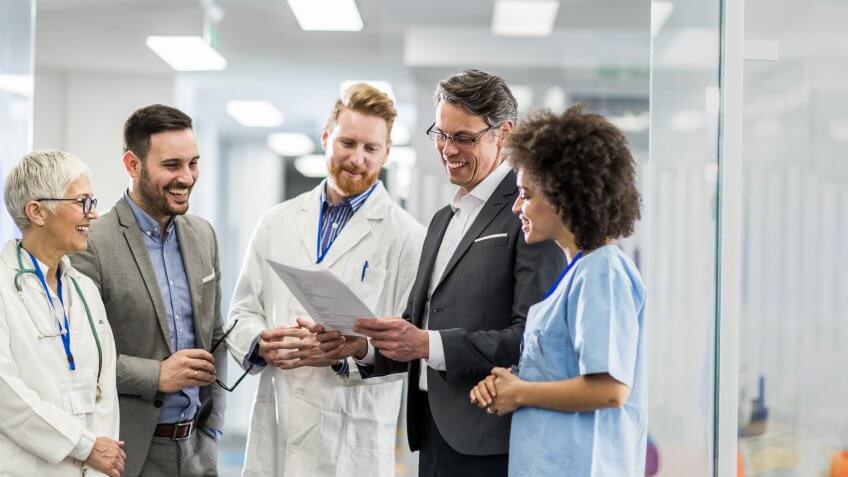 Team of happy doctors and two businessmen cooperating while going through paperwork in a hospital.