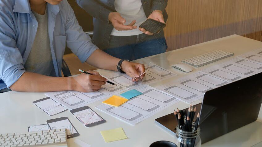Website designer planning application development draft template layout framework and coding program on paper and computer.