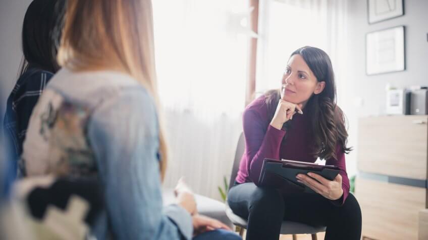 Pregnant counselor advising young lesbian couple at their home.