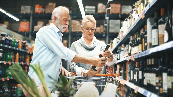 Grocery Shopping Closeup side view of early 60's couple walking through supermarket aisle and choosing some wine for tonight's dinner.