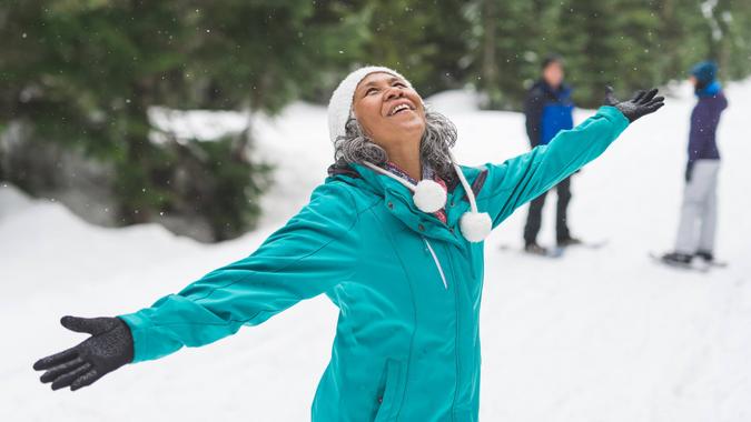 Beautiful ethnic woman in her 50s heads out for a snowshoeing adventure in the white forest with her husband and daughter, who are in the background.