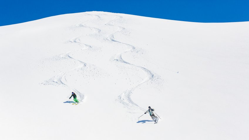 Man and woman skiing down mountain leaving tracks behind.