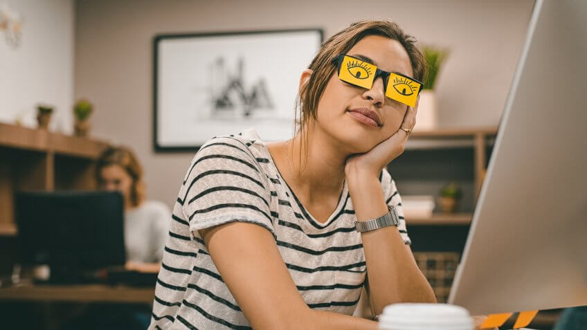 Sleeping businesswoman covering her eyes with sticky notes on eyeglasses.