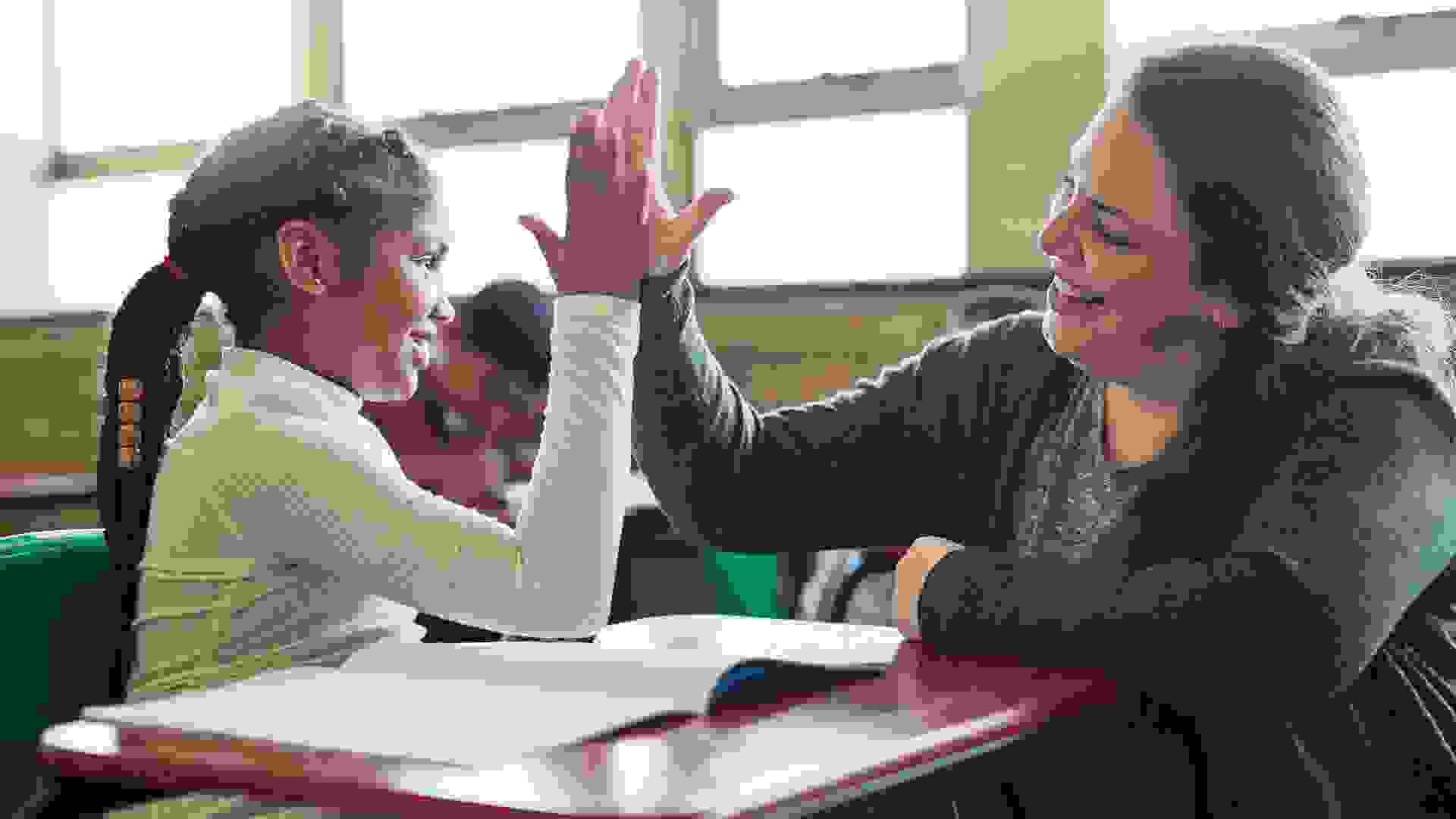 Shot of a young girl giving her teacher a high five in a classroom.