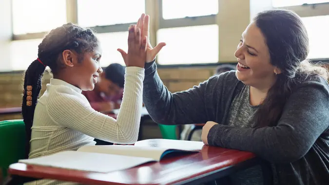 Shot of a young girl giving her teacher a high five in a classroom.