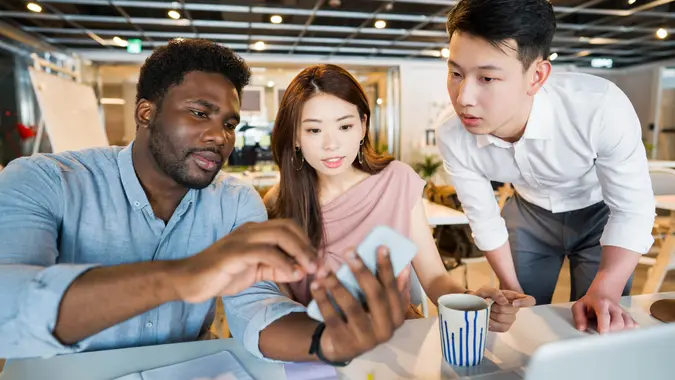 Small and young multi-ethnic group working together with computer at the desk in big office.