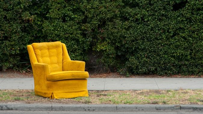A yellow vintage chair sitting on the side of a street.