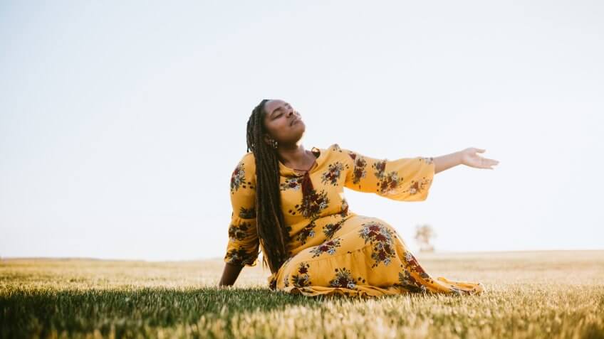 A beautiful young adult African woman enjoys the beauty of the summer , her eyes closed in prayer, worship, or meditation.