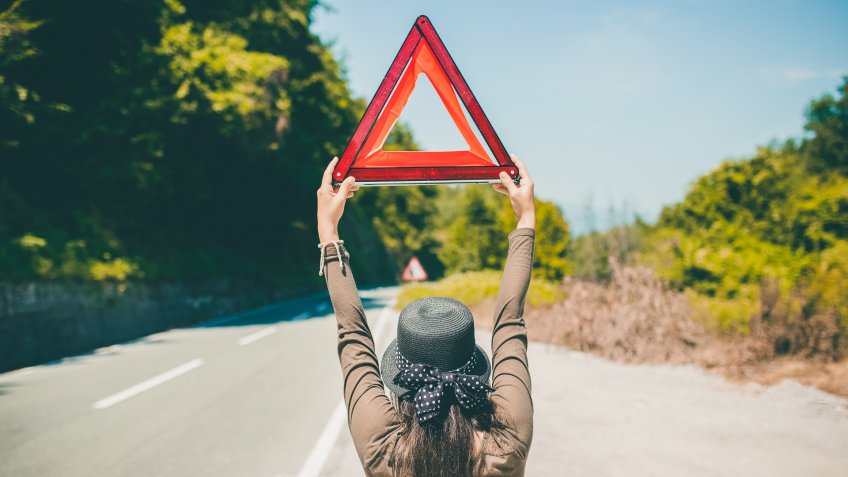 Young caucasian woman standing on a road and holding road triangle asking for help.
