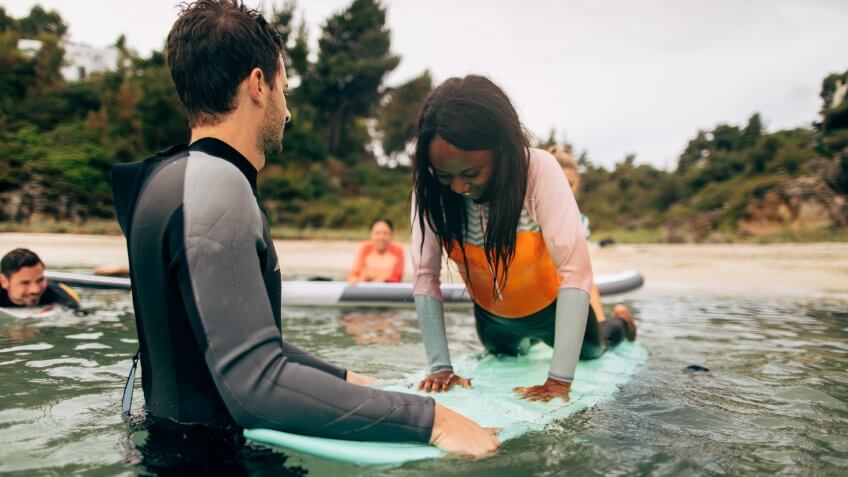 Young woman and her instructor having surfing class in the sea.