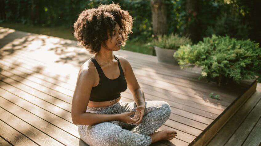 Young woman practicing yoga outdoors on porch, she enjoy in summer sun and meditation.