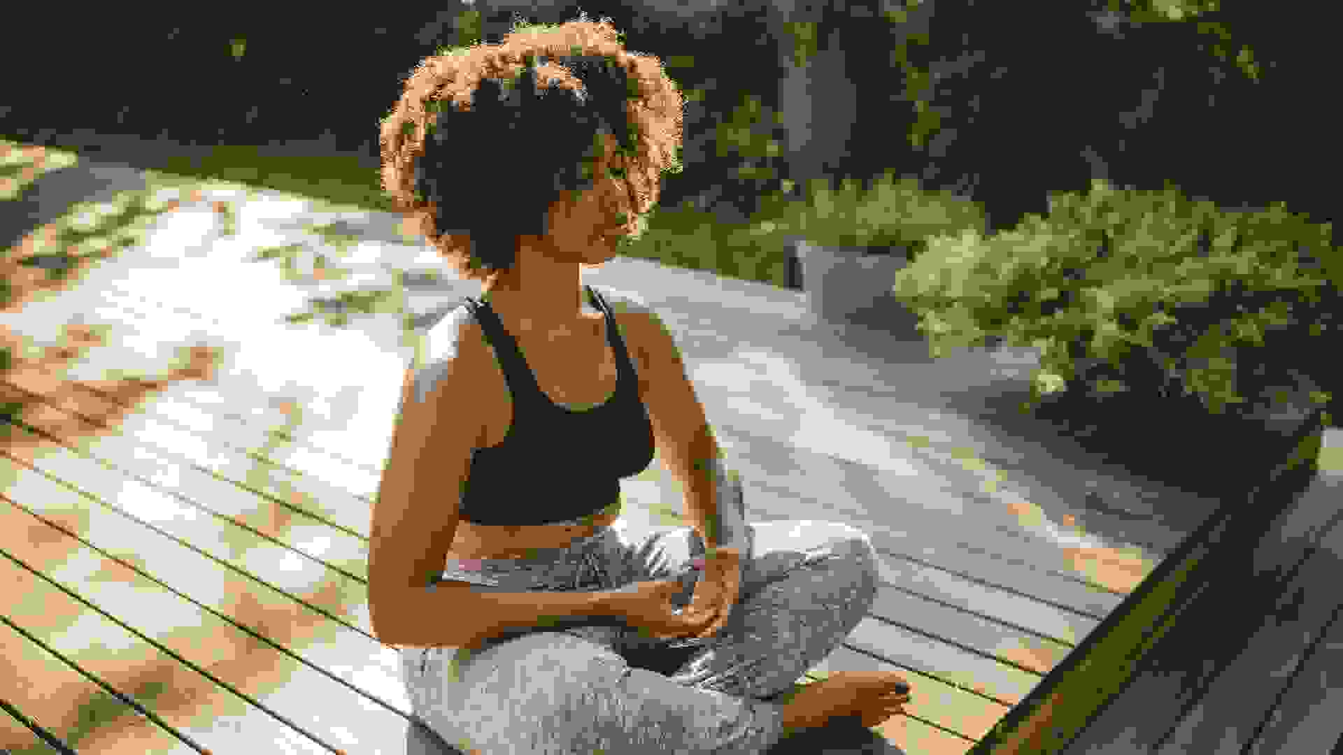 Young woman practicing yoga outdoors on porch, she enjoy in summer sun and meditation.