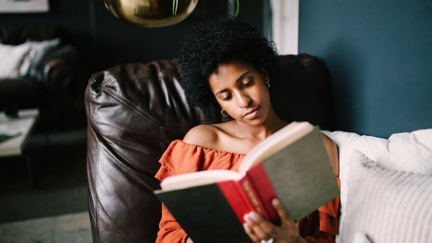 Young woman relaxing on the bed in her Downtown Los Angeles apartment, having an easy afternoon, reading a book in a warm and cozy home atmosphere.
