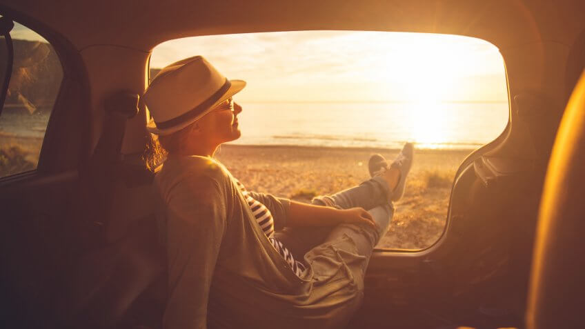 Young woman sitting in the trunk of a car on a beach in sunset.