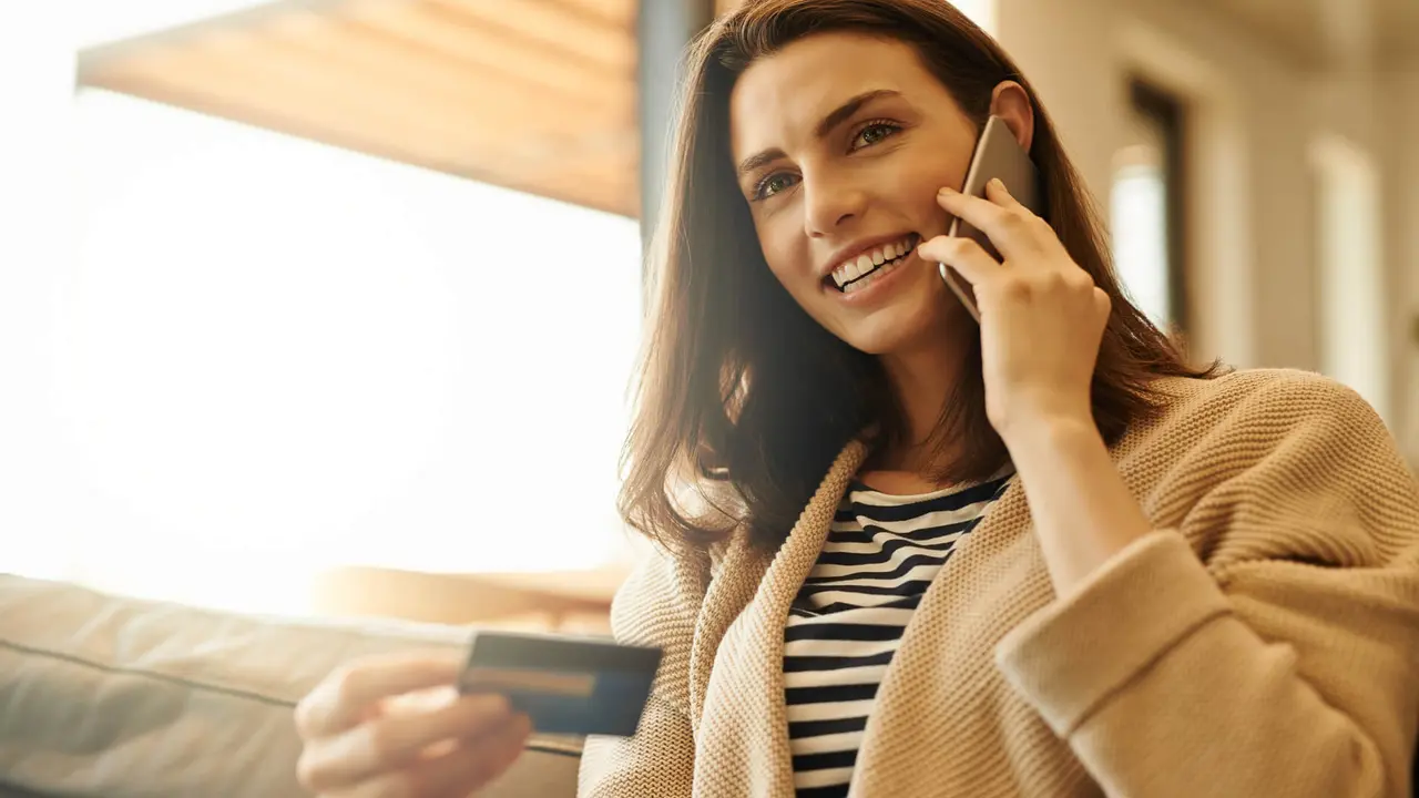 Shot of a beautiful young woman using a cellphone and credit card at home.