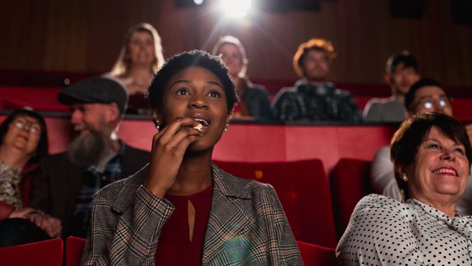 Young female adult sitting in a movie theatre and enjoying the movie while eating popcorn.