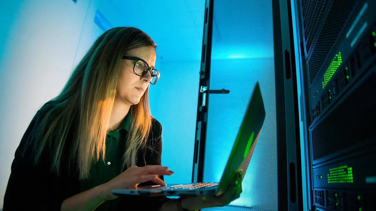 Female IT Professional Working With Laptop in Supercomputer Room.