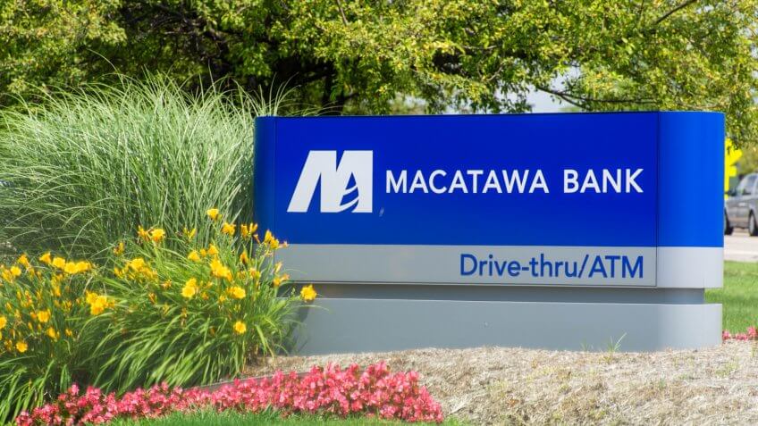 "Holland, Michigan/United States of America - 07/17/2019: Blue Macatawa Bank Sign with drive thru, atm and flowers on green grass and blue sky.