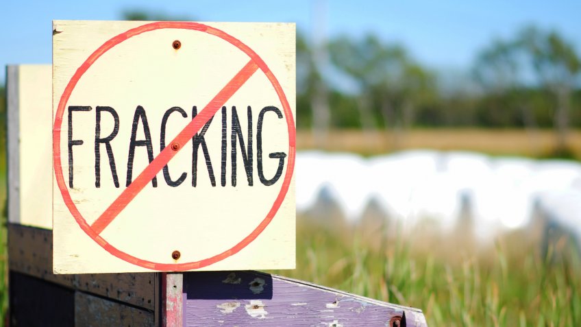Hand-painted No Fracking Sign in Rural Setting, farmland and hay bales in background.