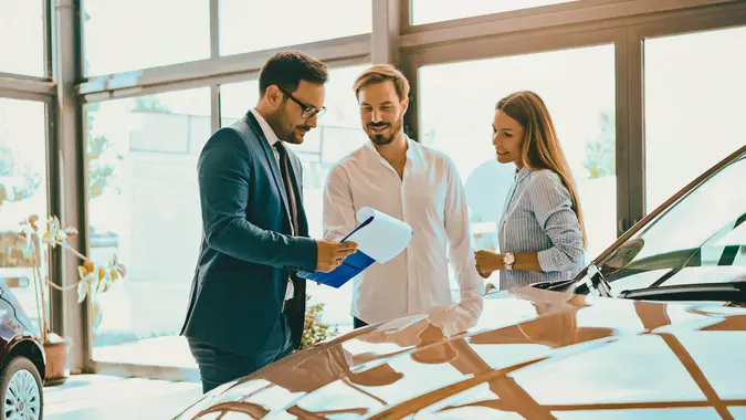 A couple buying a new car at a dealership showroom, discussing options with a sales representative.