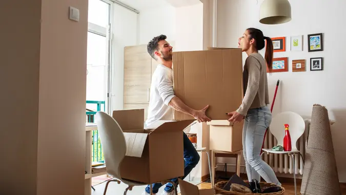 Young couple carrying big cardboard box at new home.
