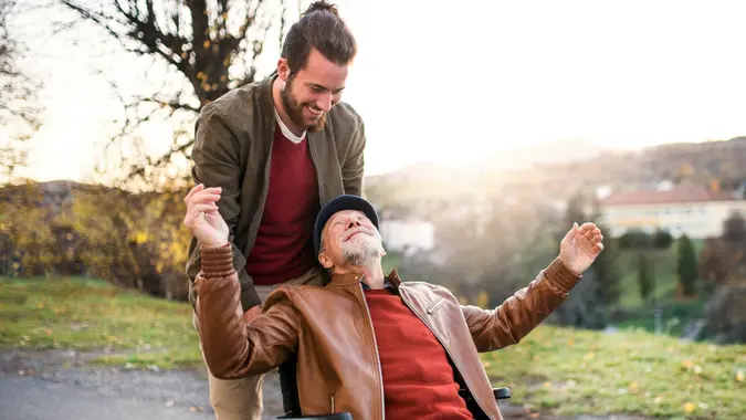 A young man and his senior father in wheelchair on a walk in town at sunset.