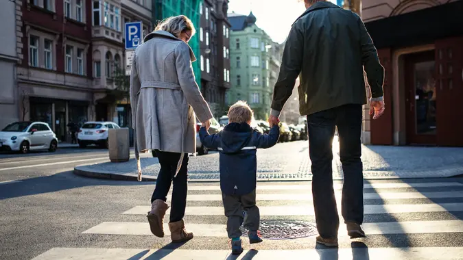 A rear view of small toddler boy with parents crossing a road outdoors in city, holding hands.