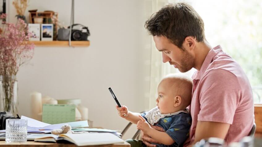 Father looking at baby boy playing with pen.