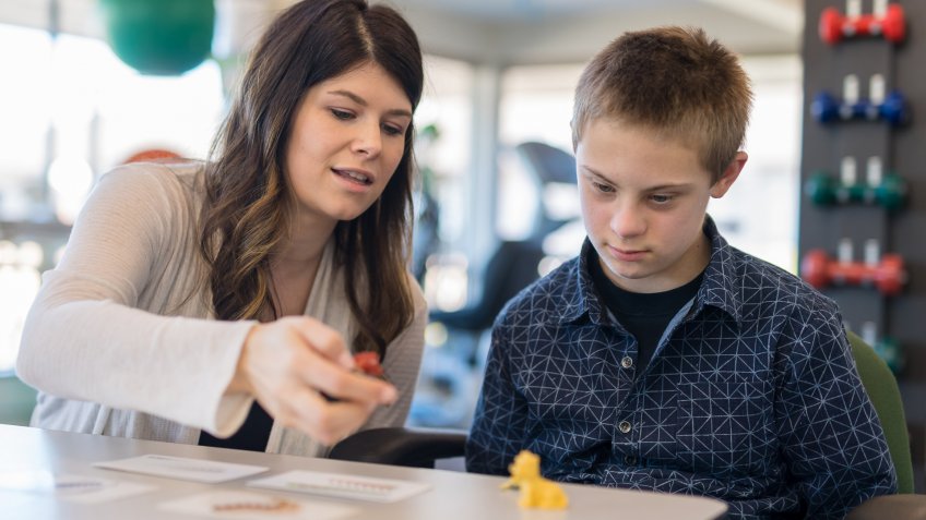 A female speech therapist works with a handsome elementary-age boy in a clinic setting.