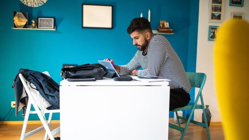 Bearded man sitting at desk and using touch screen device for freelance work at home.