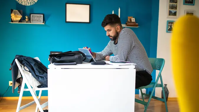 Bearded man sitting at desk and using touch screen device for freelance work at home.