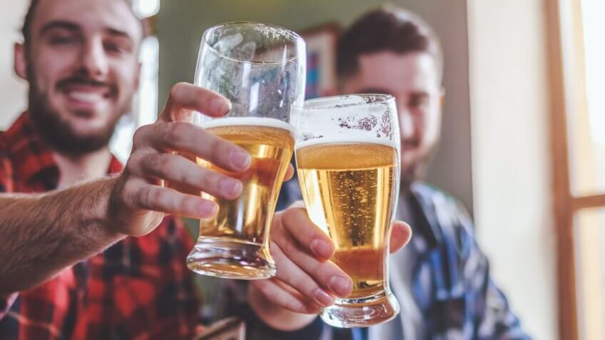 Two bearded hipsters clinking glasses of beer at bar.