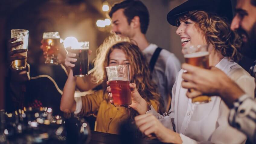 Group of friends sitting in a pub, drinking beer at the bar counter.