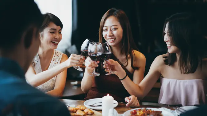 Group of joyful young Asian woman having fun and toasting with red wine during party.