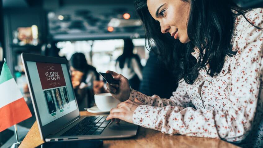 Beautiful young woman shopping online using laptop in cafe.
