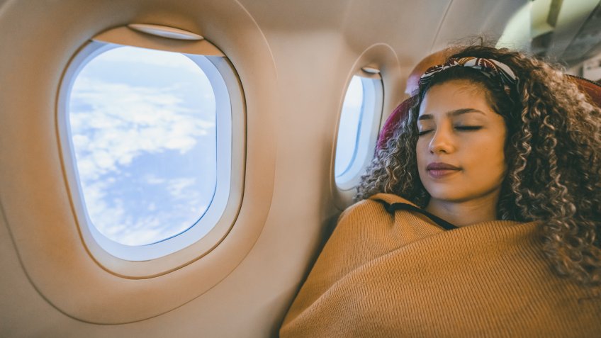 Portrait of a beautiful woman traveling by plane and sleeping during the flight - travel concepts.