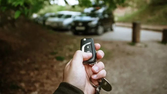 A human hand holding car keys to open a car.