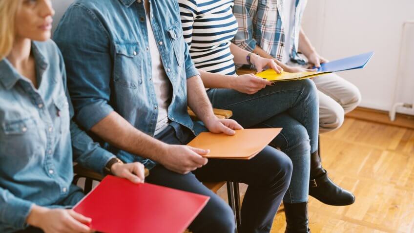 Close up view of young people sitting in chairs with folders before the job interview in the waiting room.