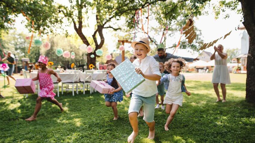 Small children ruunning with present outdoors in garden on birthday party, playing.