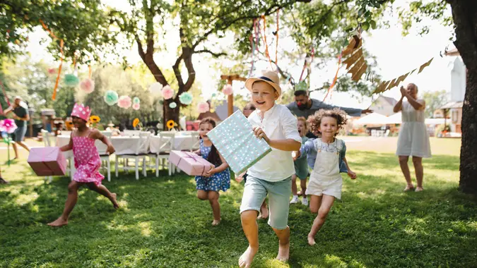 Small children ruunning with present outdoors in garden on birthday party, playing.